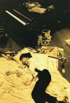 a man laying in bed next to a pile of papers and a piano on the floor