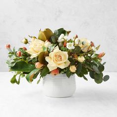 a white vase filled with yellow flowers and greenery