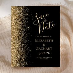 black and gold wedding save the date card with glitter on it, sitting on a white blanket