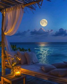 a full moon is seen over the ocean at night with candles lit up in front of it