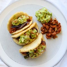 three tacos with guacamole and beans on a white plate, ready to be eaten