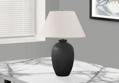 a black vase sitting on top of a white table next to a lamp and window