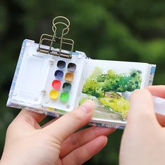 a person holding an open book with watercolors on it and a brush in their hand