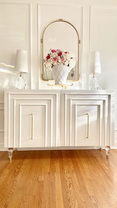 a white sideboard with flowers on top and a mirror above it in a living room