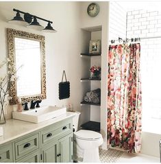 a bathroom with a floral shower curtain next to a white sink and green cabinetry