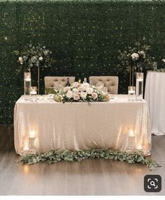 a table with candles and flowers on it in front of a wall covered in greenery