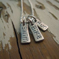 three silver necklaces with words on them sitting on a wooden surface and hanging from a chain