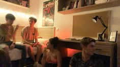 four people sitting on a bed in a room with bookshelves and desks