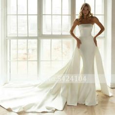 a woman in a white wedding dress standing by a window with her hands on her hips