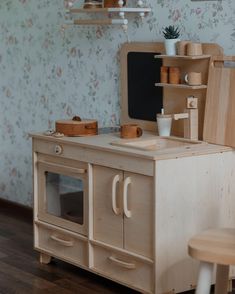 a wooden toy kitchen set in a room with floral wallpaper and wood flooring