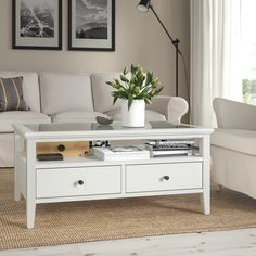 a white coffee table with two drawers and a vase on it in front of a couch