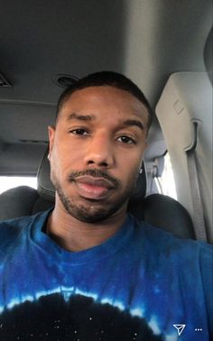 a man sitting in the back seat of a car wearing a tie dye t - shirt