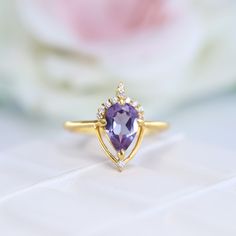 an amethorate and diamond ring sits on top of a white cloth with flowers in the background