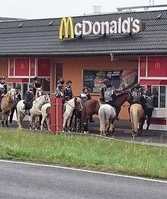 a group of people riding horses in front of a mcdonald's