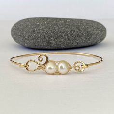 Peas in a pod gold bangle bracelet.   Handmade with 14/20 gold filled wire and two white freshwater pearls. Each peapod charm is weaved together.  The spirals are hand formed and hammered to give them a little bit of a flared look before being attached to the bangle. The peas in a pod charm measures approximately 1.24" pearls are about 7mm. My Favorite part about this gold bangle bracelet is that it features a hook closure that makes this bangle easy to put on and take off.  No worries about trying to slip it over your knuckle I individually hand make each and every gold filled bracelet, there will be slight variations, making each one truly one of a kind. Wether you are treating yourself or buying a jewelry gift for someone. This peas in a pod bangle would make a great gift for any specia Adjustable Wire Wrapped Bracelet For Anniversary, Handmade Adjustable Yellow Gold Pearl Bracelet, Adjustable Handmade Yellow Gold Pearl Bracelet, Gold Wire Wrapped Cuff Bracelet Gift, Gold Wire Wrapped Bangle For Gift, Wire Wrapped Bangle Jewelry For Anniversary, Adjustable Brass Bracelets For Anniversary, Wire Wrapped Gold Bangle Bracelet As Gift, Wire Wrapped Brass Bracelets Gift