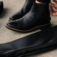 a person wearing black boots with their foot on the ground next to another pair of shoes