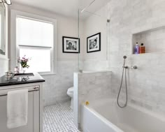 a white bathroom with black and white flooring, framed pictures on the wall above the bathtub