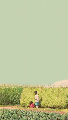 two people standing in the middle of a field with green plants on either side of them