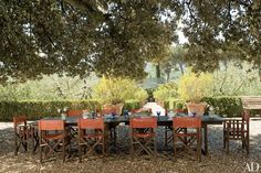 a table and chairs under a tree in the middle of a gravel area with benches