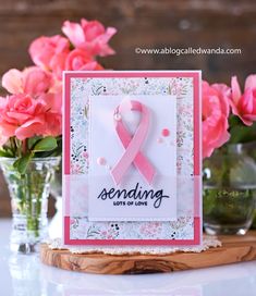 a card with pink ribbon and flowers in vases next to it on a table