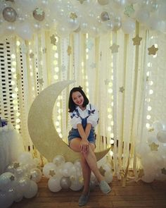 a woman is sitting on the moon in front of balloons and streamers with stars