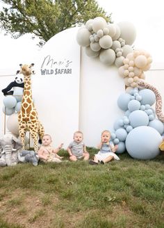 two babys are sitting in the grass with balloons and giraffes