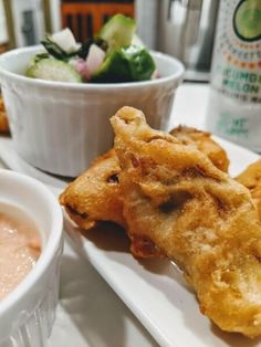 some food is sitting on a white plate near a bowl of dipping sauce and a cup of salad