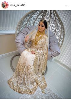 a woman in a white and gold sari sitting on a chair with her head covered by a veil