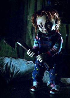 a creepy doll is holding a knife in the dark, while sitting on a bed