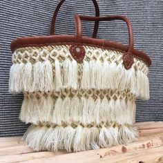 a woven purse with leather handles and tassels hanging on a wooden shelf next to a wall