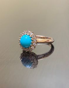 a ring with a turquoise stone in the center on a reflective surface, showing its reflection