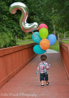 a young boy holding balloons on a bridge with the number 3 balloon attached to it