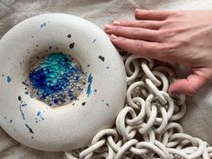 a person is holding a bowl with blue and white paint on it next to chains