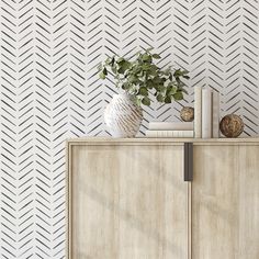 a white vase sitting on top of a wooden cabinet next to a wall with geometric designs