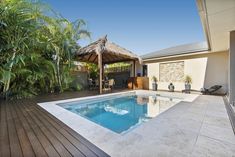 an outdoor swimming pool surrounded by greenery and a gazebo with thatched roof