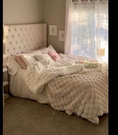 an unmade bed with white sheets and pillows in a bedroom next to a window