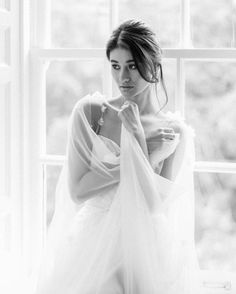 black and white photograph of a woman wearing a wedding dress in front of a window