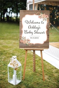 a baby shower sign sitting on top of a grass covered field next to a small white house