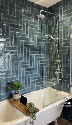 a bath tub sitting under a window next to a shower head and a laptop on a wooden tray