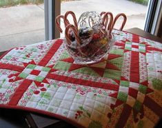 a glass bowl filled with candy canes on top of a red and green table cloth