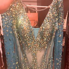 a blue dress with sequins on it is being held up by someone's hand