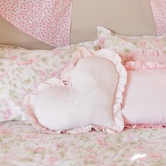 a heart shaped pillow sitting on top of a bed next to two pillows with the word love written on them