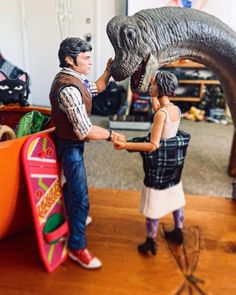 two figurines are holding hands in front of a fake dinosaur's mouth