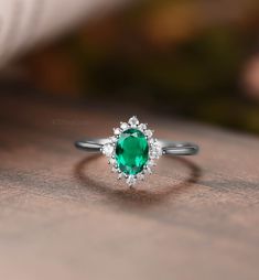 an emerald and diamond ring sitting on top of a wooden table