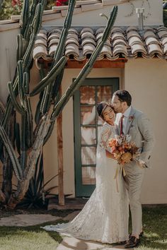 a bride and groom standing in front of a house with cacti on the roof