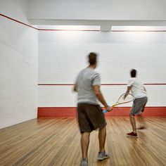 two men are playing tennis in an empty room with hard wood floors and white walls