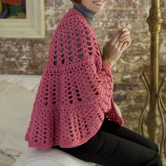 a woman sitting on top of a white couch wearing a pink crocheted shawl