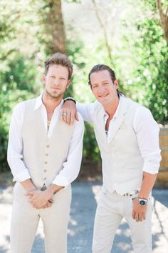 two men standing next to each other in white suits and ties, one is holding his arm around the other man's shoulder