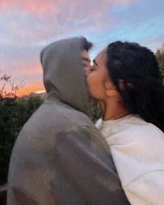 a man and woman kissing in front of a sunset