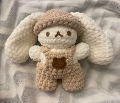 a crocheted teddy bear laying on top of a bed with white and brown blankets